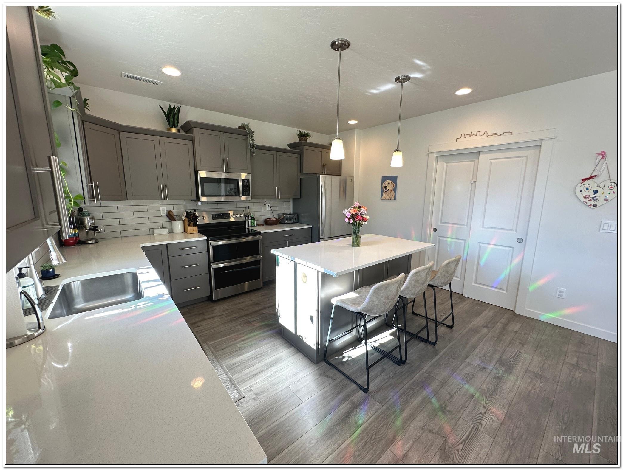 9687 West Arnold Road Boise, ID 83714 - Photo 4 of 49 Kitchen with stainless steel appliances, hanging light fixtures, a center island, and light stone counters