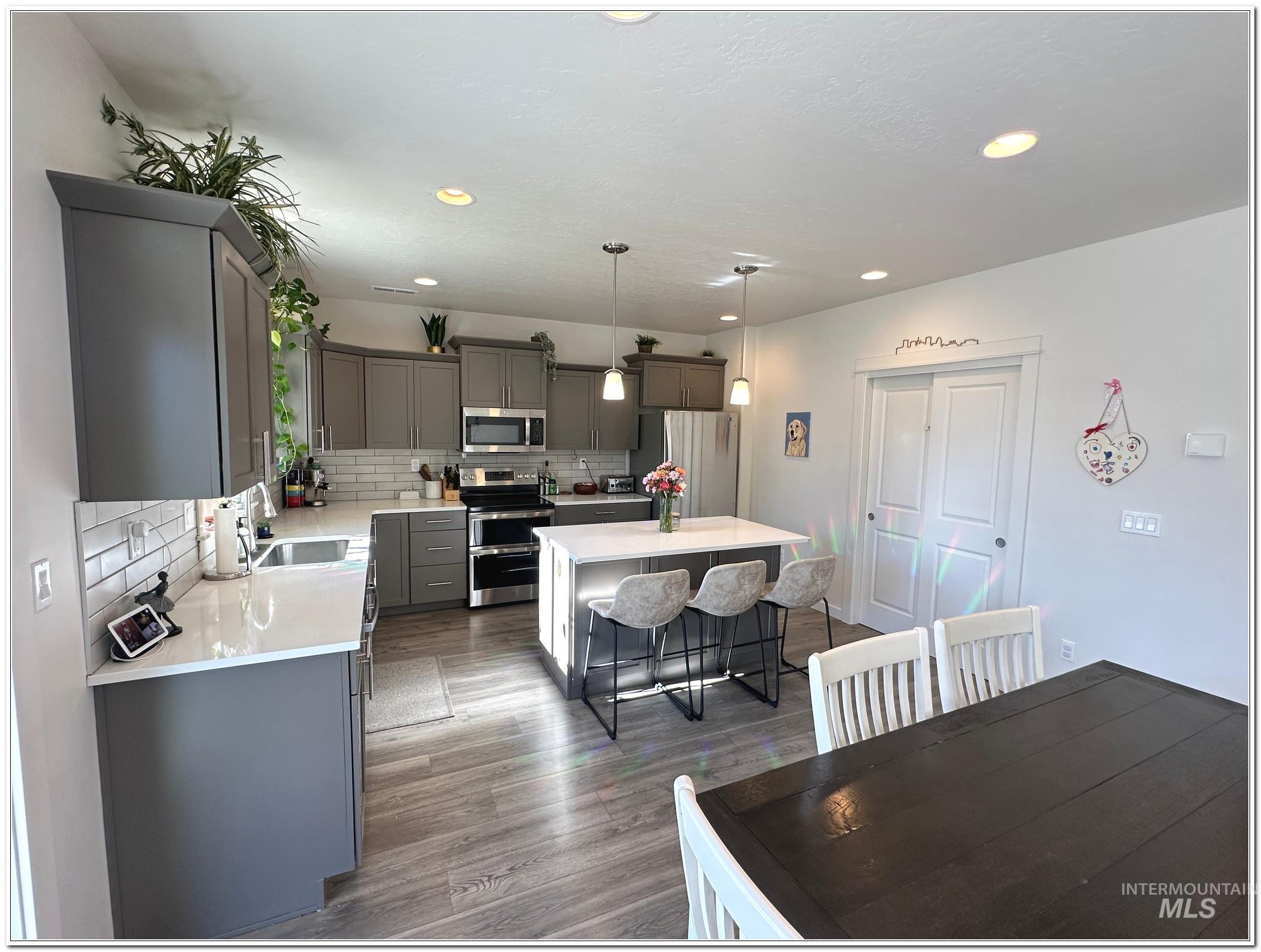 9687 West Arnold Road Boise, ID 83714 - Photo 6 of 49 Kitchen with hanging light fixtures, stainless steel appliances, a kitchen island, tasteful backsplash, and dark wood-type flooring