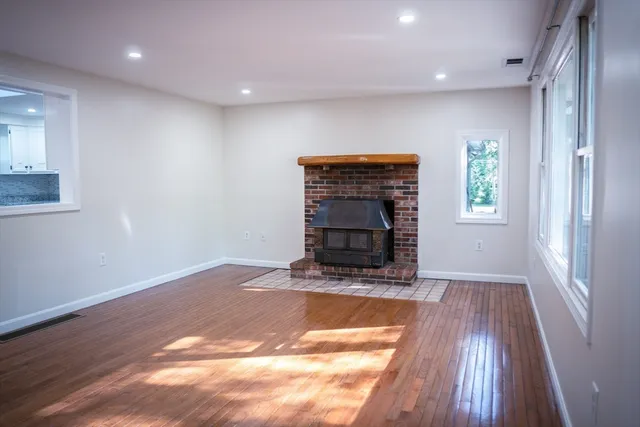 a view of an empty room with wooden floor fireplace and a window