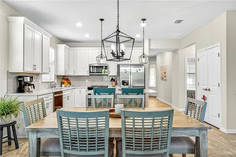 a open kitchen with stainless steel appliances granite countertop a stove top oven a refrigerator a sink dishwasher a dining table and chairs with wooden floor