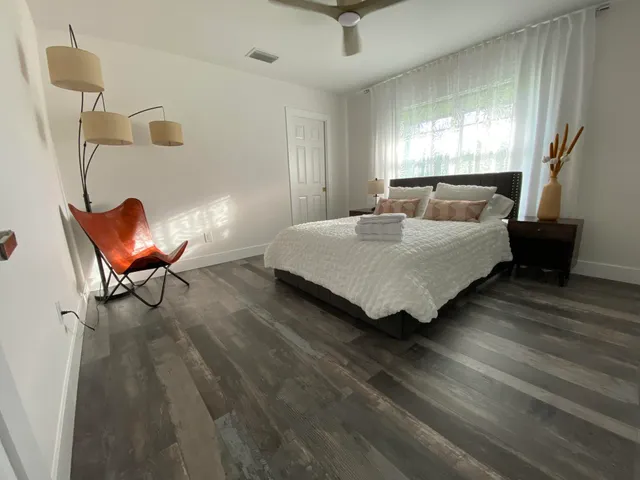 a bedroom with a bed a chair and potted plant on the dresser