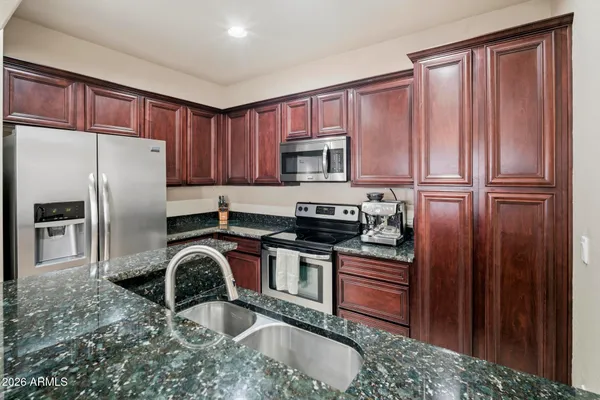 a kitchen with stainless steel appliances granite countertop a refrigerator a stove and a sink with wooden cabinets
