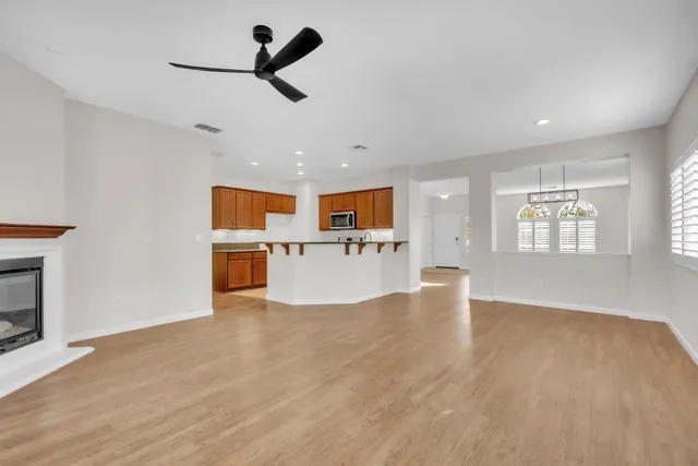 an empty room with wooden floor kitchen view and windows
