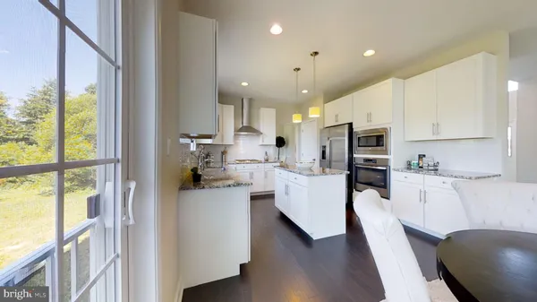 a kitchen with stainless steel appliances kitchen island granite countertop a refrigerator a stove and white cabinets with wooden floor