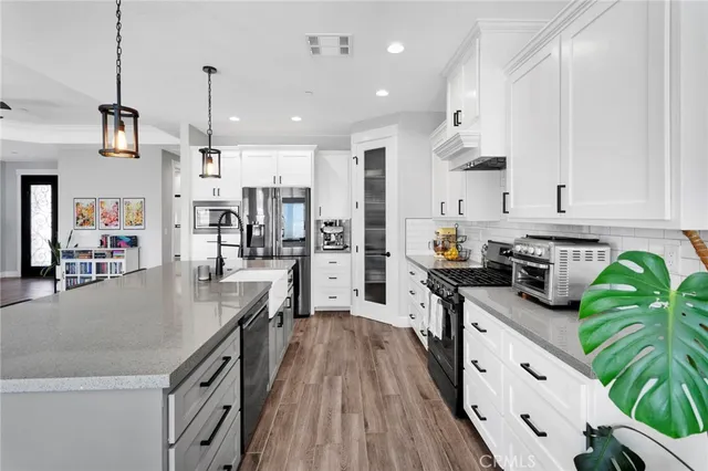 a kitchen with stainless steel appliances granite countertop a refrigerator a stove top oven a sink dishwasher and white cabinets with wooden floor