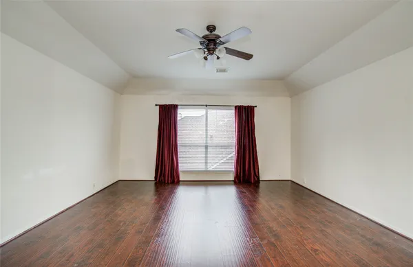 an empty room with wooden floor chandelier fan and windows