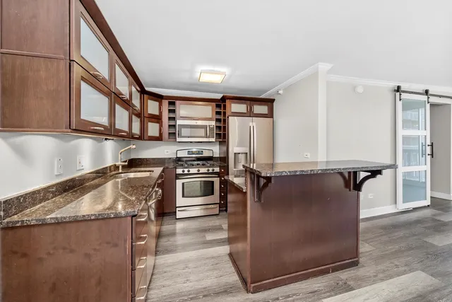 a kitchen with stainless steel appliances granite countertop a refrigerator a stove and a sink with wooden floors