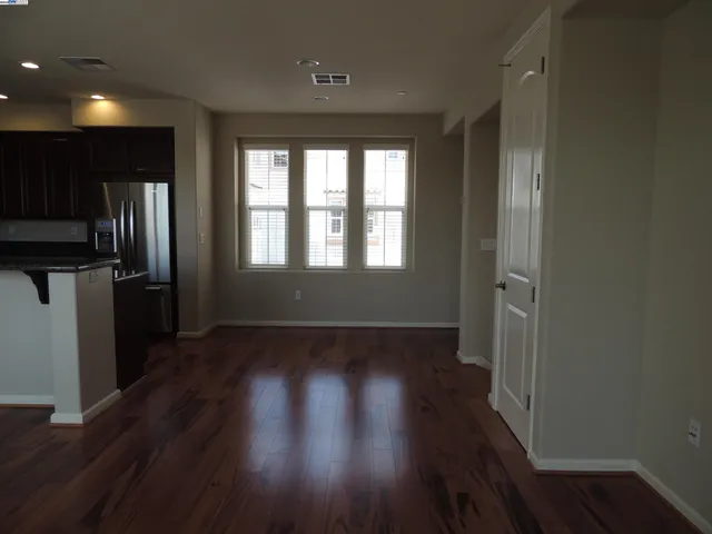 an empty room with wooden floor and a kitchen