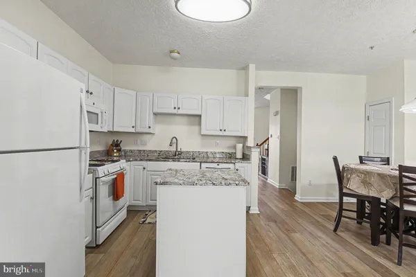 a kitchen with stainless steel appliances granite countertop a stove top oven a sink a dining table and chairs with wooden floor