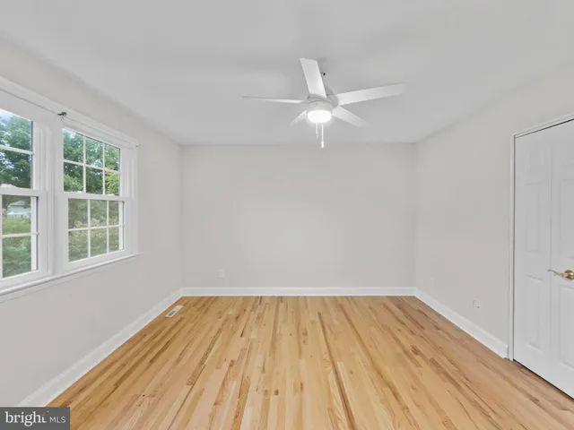an empty room with wooden floor fan and windows