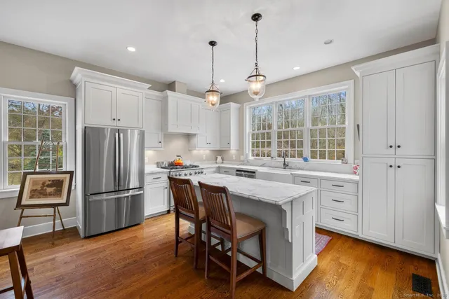 a kitchen with stainless steel appliances granite countertop a refrigerator a stove a sink dishwasher a dining table and chairs with wooden floor