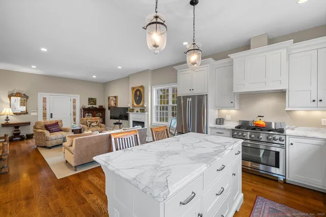 a kitchen with stainless steel appliances kitchen island granite countertop a stove top oven a refrigerator a sink dishwasher and white cabinets with wooden floor