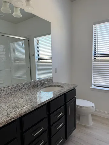 a bathroom with a granite countertop sink a toilet and a window