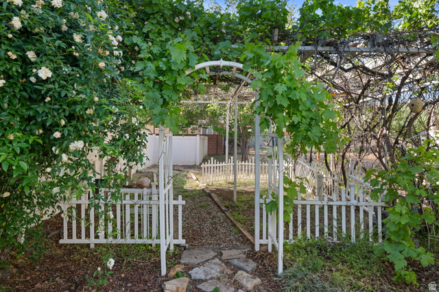 20 Valley Road Leeds, UT 84746 - Photo 29 of 57 Garden entry featuring a white arched arbor, mature climbing foliage, white picket fencing, and stepping stones