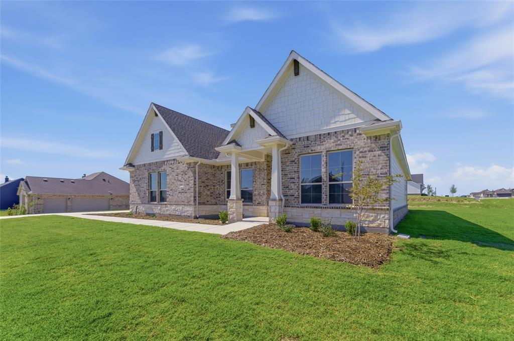 104 Snowy Owl Trail Rhome, TX 76078 - Photo 4 of 27 Single-story residence featuring a brick and stone facade, gabled rooflines with shingle siding accents, a covered entry with columns, and a landscaped front yard with a concrete pathway