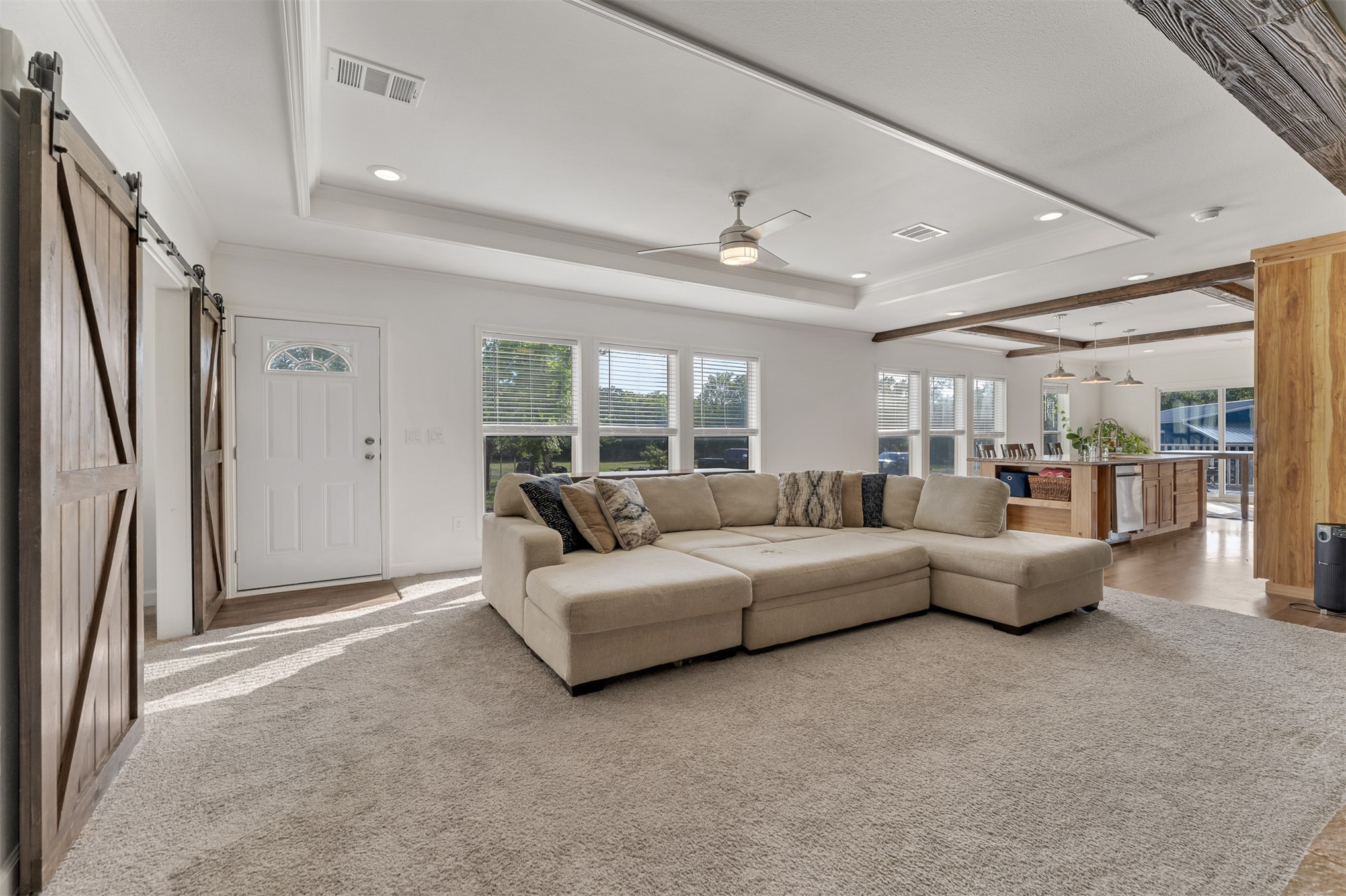 15291 East 400 Road Claremore, OK 74017 - Photo 34 of 96 Tray ceiling with recessed lighting, wood-finish barn doors, multiple windows, exposed wood beams, and a ceiling fan