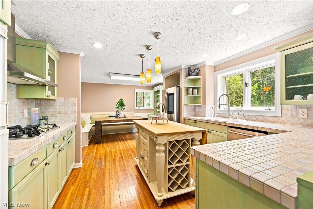 Kitchen featuring green cabinetry, wood-finish flooring, a central island with wine storage, stainless steel appliances, and a built-in banquette