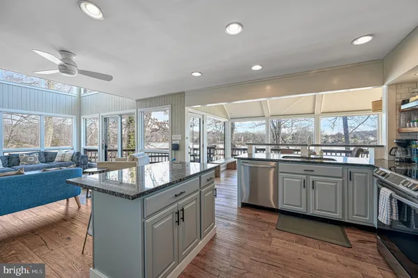a kitchen with stainless steel appliances granite countertop a table chairs wooden floors and a view of living room