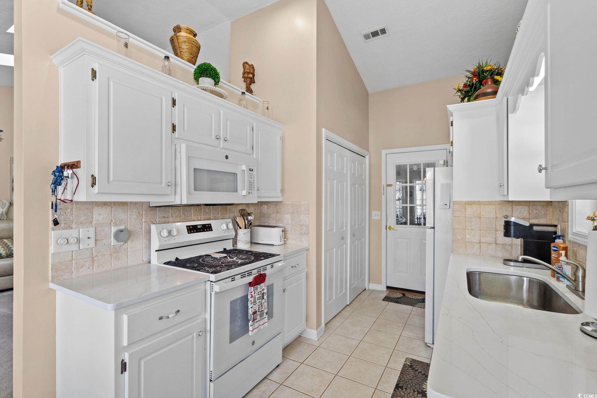 9533 Sullivan Drive Murrells Inlet, SC 29576 - Photo 14 of 40 Kitchen with decorative backsplash, white appliances, white cabinets, and light tile patterned floors