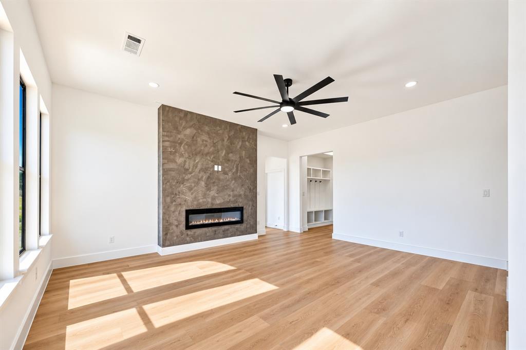 1632 West Wintergreen Road Lancaster, TX 75134 - Photo 12 of 30 Wood-finish flooring, a linear electric fireplace with a textured accent wall, multiple large windows, and a ceiling fan with integrated lighting