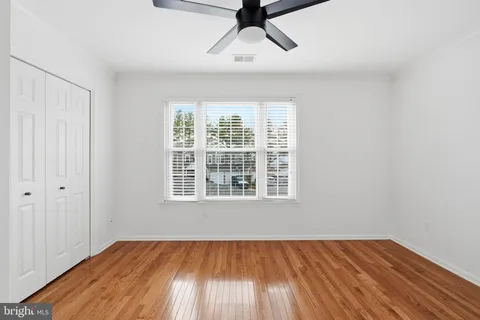 an empty room with wooden floor a ceiling fan and windows