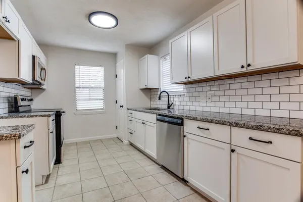 a kitchen with granite countertop white cabinets stainless steel appliances a sink and a window