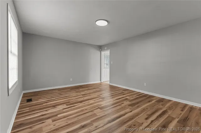 a view of an empty room with wooden floor and a window