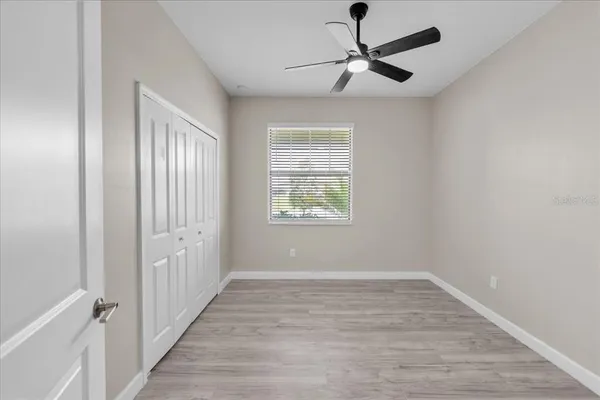 an empty room with wooden floor chandelier fan and windows in a room