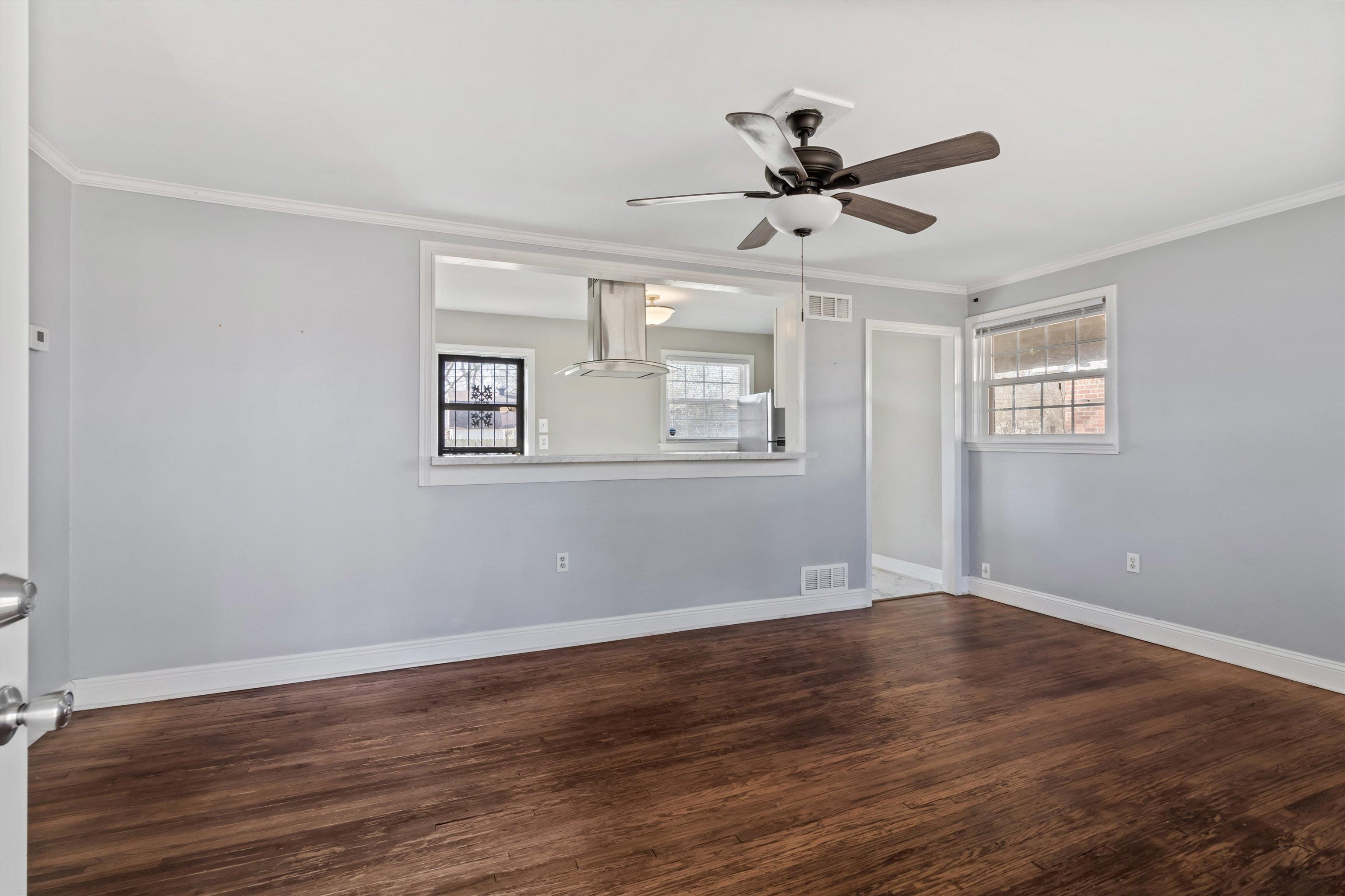 517 Malboro Road Memphis, TN 38120 - Photo 4 of 25 Empty room featuring dark wood-style flooring, a ceiling fan, crown molding, and healthy amount of natural light