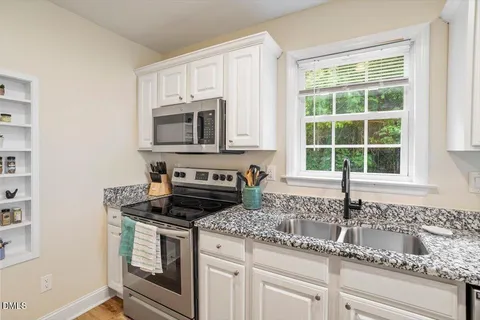 a kitchen with granite countertop white cabinets appliances and a window