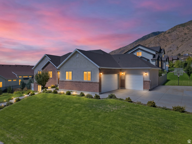 1997 East 600 South Springville, UT 84663 - Photo 48 of 54 Stucco and brick exterior with a dark shingle roof, attached two-car garage, concrete driveway, and an expansive lawn with landscape lighting