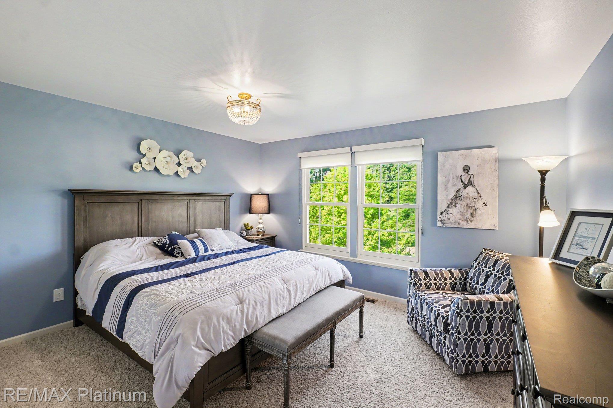 609 Telya Ridge Milford, MI 48381 - Photo 16 of 28 Serene primary bedroom showcasing soft blue walls, wood-finish flooring, and abundant natural light from dual glass doors overlooking mature landscaping