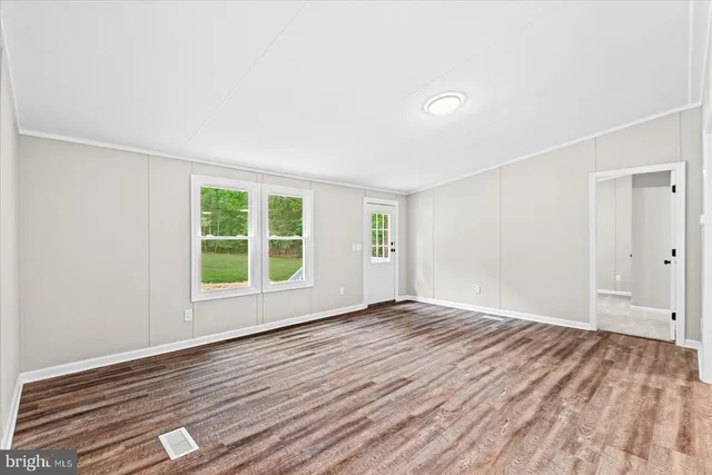 a view of an empty room with wooden floor and a window