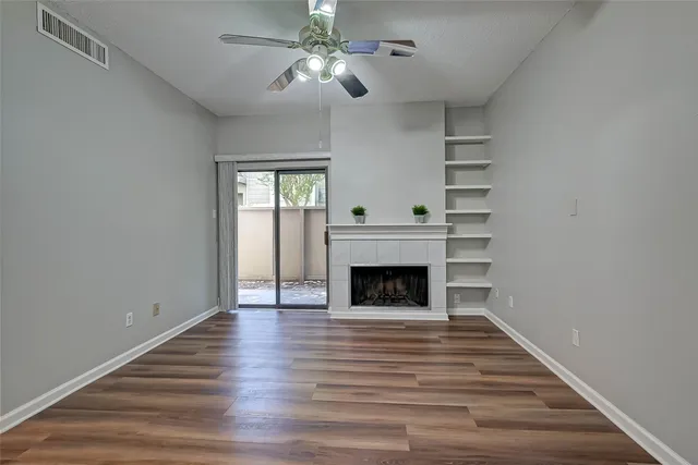 a view of an empty room with wooden floor fireplace and a window