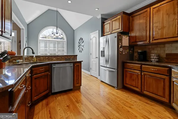 a kitchen with stainless steel appliances granite countertop a refrigerator a sink dishwasher and wooden cabinets with wooden floor