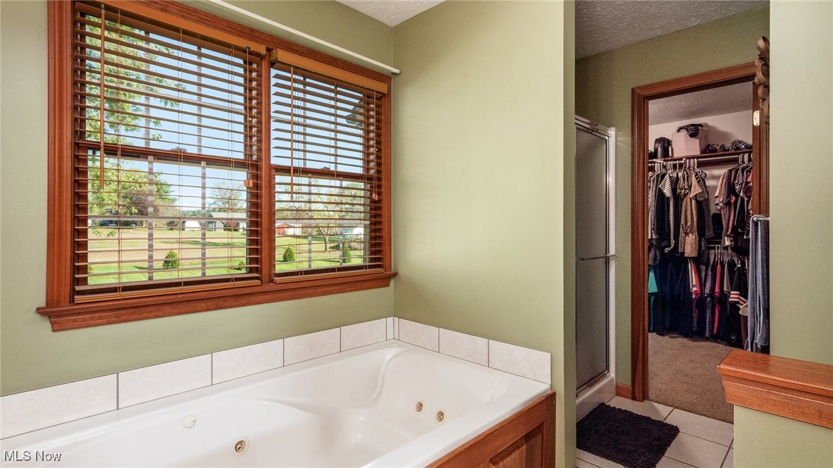 62960 James Road Cambridge, OH 43725 - Photo 22 of 40 Bathroom with a shower stall, a jetted tub, light tile patterned flooring, a walk in closet, and a textured ceiling