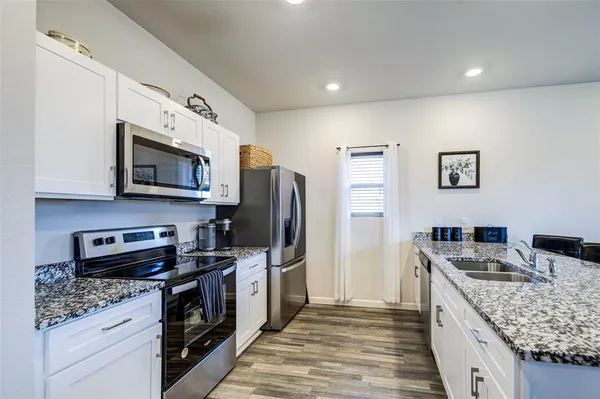 a kitchen with stainless steel appliances granite countertop a stove top oven a sink dishwasher a refrigerator and a microwave oven with large trees
