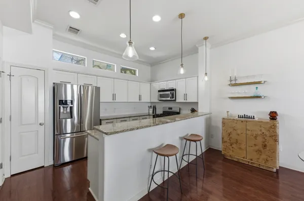 a kitchen with stainless steel appliances granite countertop a refrigerator a sink dishwasher a stove and white cabinets with wooden floor