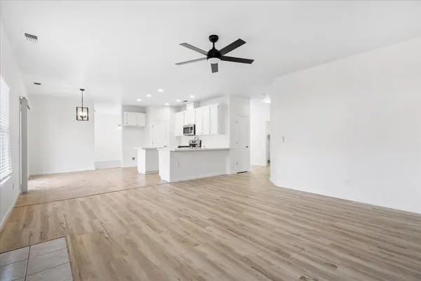 a view of an empty room with kitchen appliances and a ceiling fan