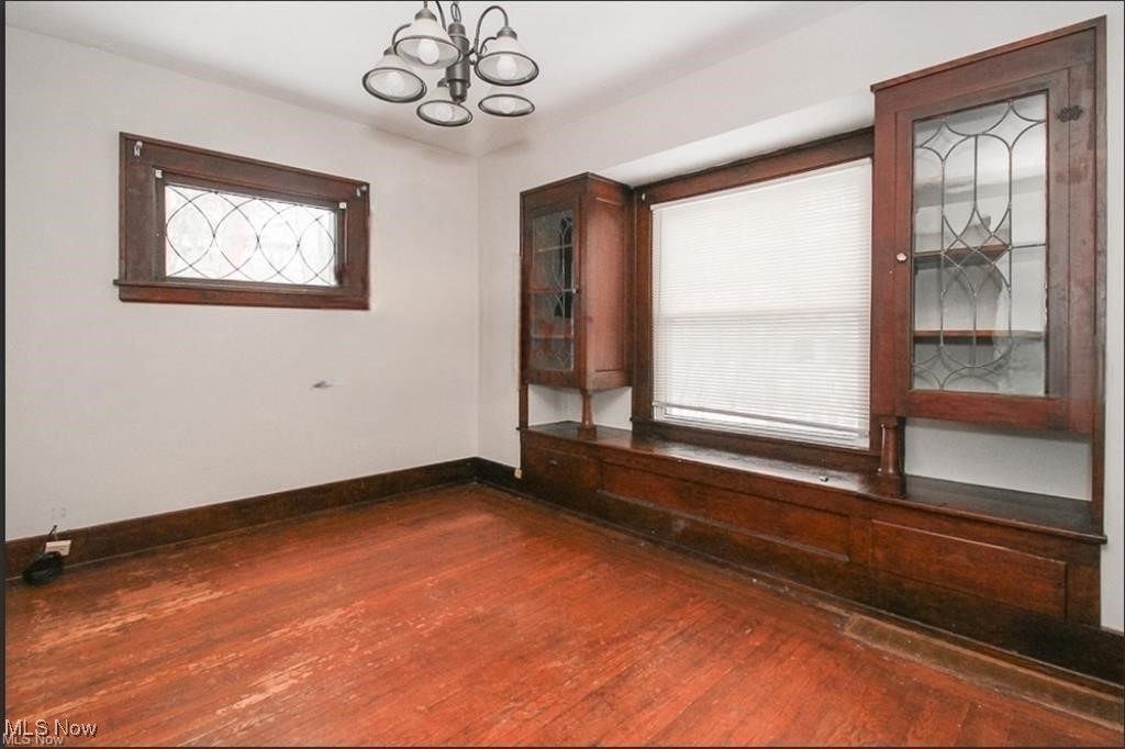 Unfurnished room featuring an inviting chandelier, baseboards, and dark wood finished floors