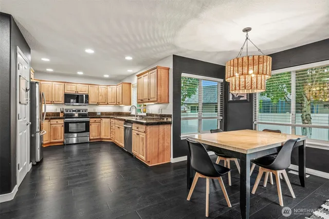 a kitchen with stainless steel appliances granite countertop a stove top oven a sink dishwasher a dining table and chairs with wooden floor