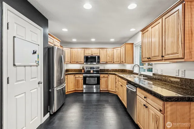 a large kitchen with stainless steel appliances granite countertop a refrigerator a sink dishwasher a stove and white cabinets with wooden floor