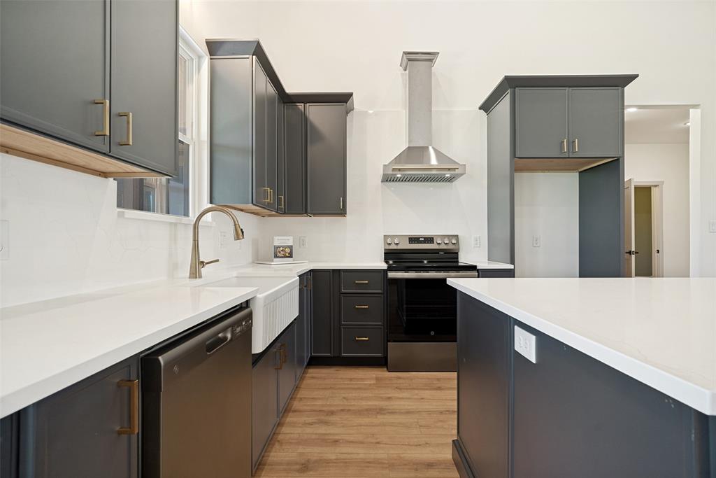 1150 Doss Road Millsap, TX 76066 - Photo 14 of 32 Modern kitchen featuring white countertops, dark gray cabinetry with brass hardware, wood-finish flooring, a stainless steel range hood, and a white farmhouse sink