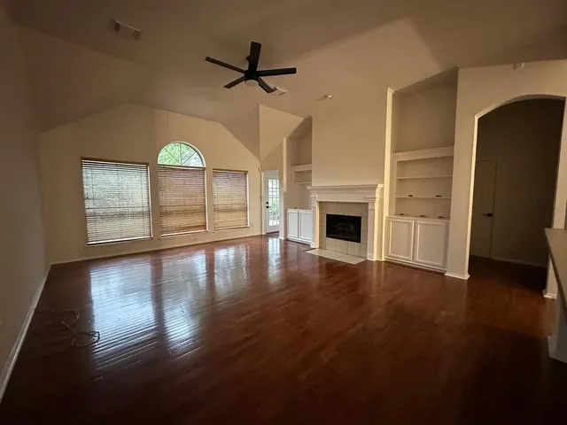 an empty room with wooden floor fireplace and windows