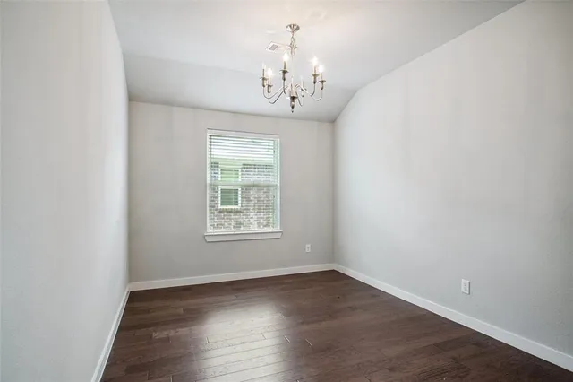 an empty room with wooden floor chandelier and window