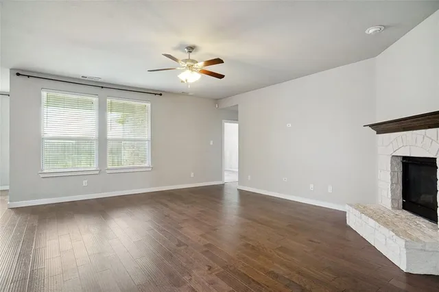 a view of an empty room with wooden floor fireplace and a window