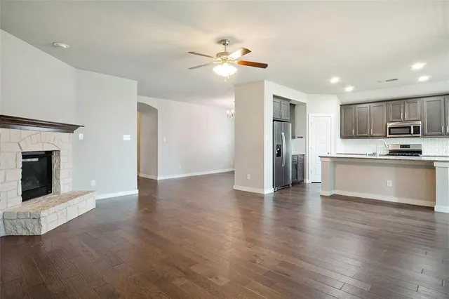 a view of an empty room with wooden floor and a kitchen