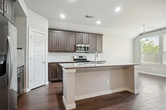 a kitchen with stainless steel appliances granite countertop a stove a sink and a refrigerator with wooden floor