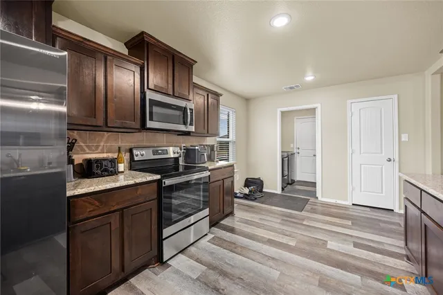 a kitchen with stainless steel appliances granite countertop a stove top oven a sink dishwasher a dining table and chairs with wooden floor