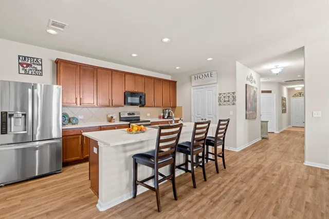 a kitchen with stainless steel appliances granite countertop a refrigerator a stove a sink a dining table and chairs with wooden floor